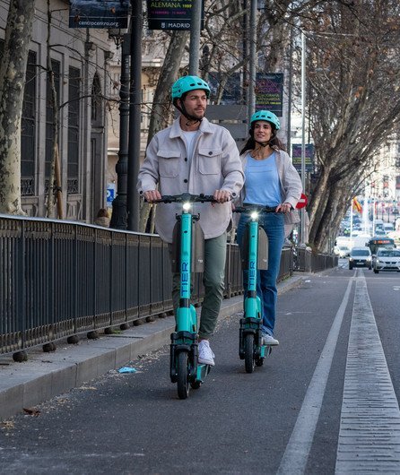 zwei Jugendliche fahren auf dem Gehsteig mit Trottinetts zum Mieten